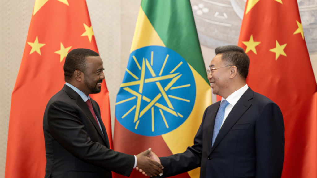 An Ethiopian & Chinese men shaking hands with smile infront of their flags